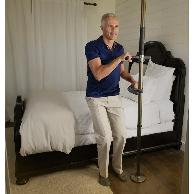Floor-to-ceiling support pole with two handles, gripped by a man standing beside a bed in a bedroom setting