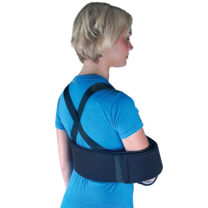 Shoulder sling and swathe brace worn by a woman in a blue shirt, shown from behind with cross-back straps