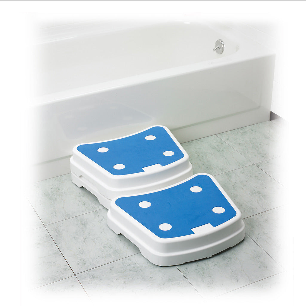 Portable bath step with blue non-slip surface and white plastic base, shown in two stackable pieces beside a bathtub