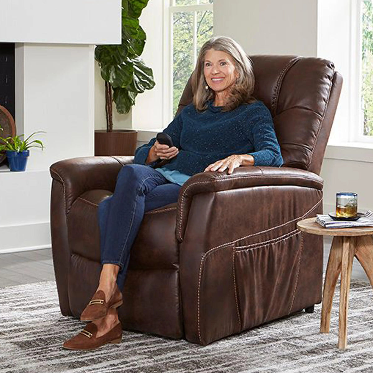 Power lift recliner chair in brown upholstery with side pocket, shown with older woman seated holding a remote control