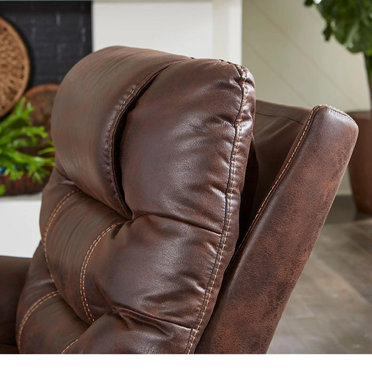 Lift chair close-up showing padded brown faux-leather headrest and armrest with contrast stitching, reclined in a home