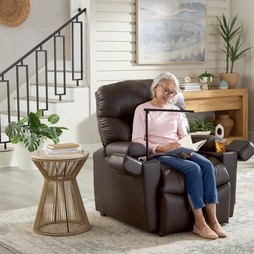 Power lift recliner in dark brown upholstery with elderly woman reading a book, shown with swivel tray and cup holder in