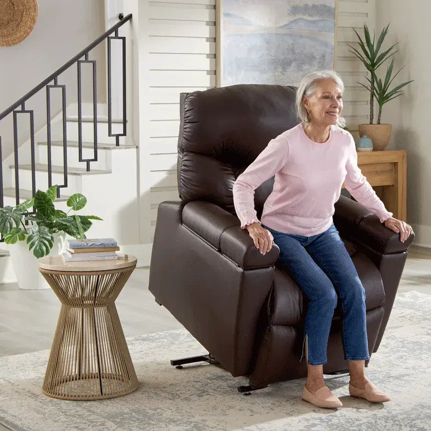 Power lift recliner in dark brown upholstery shown in raised position with older woman seated, set in a bright living room