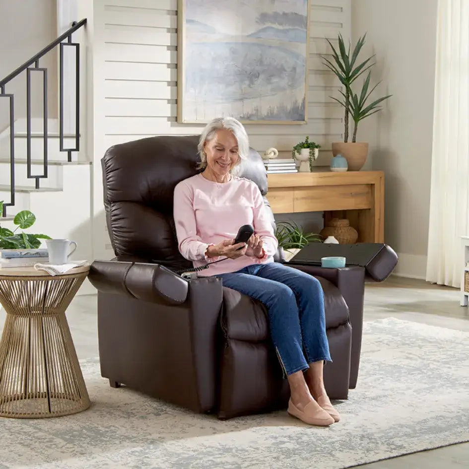 Power lift recliner in dark brown upholstery with older woman seated, holding a wired remote control, in a home living room