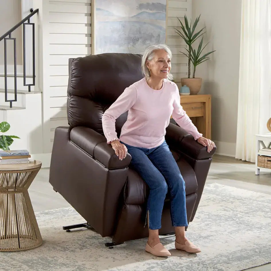 Power lift recliner in dark brown faux leather shown in raised position with older woman seated, set in a bright living room