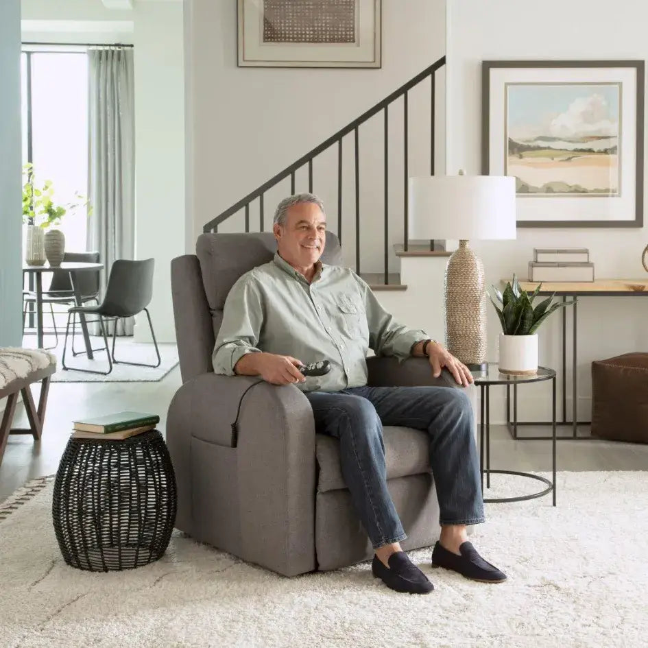 Power lift recliner chair in gray upholstery with a man seated holding a hand control in a modern living room