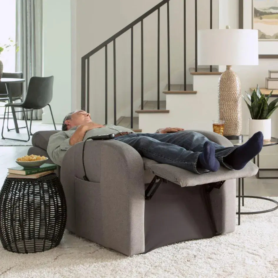 Power lift recliner chair fully reclined in flat sleeping position with man resting in gray upholstered chair holding a hand