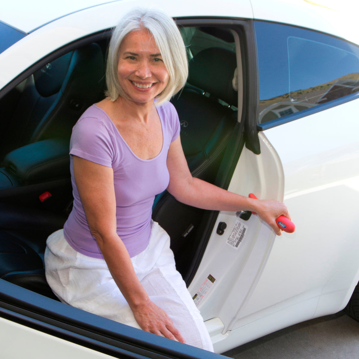 Car safety handle being used by a smiling woman to steady herself while exiting a white car, shown gripped in door latch