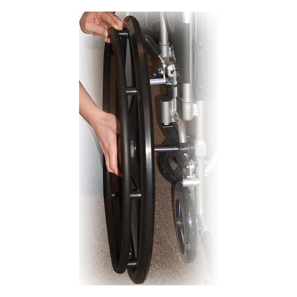 Wheelchair rear wheel being removed by hand, showing quick-release axle mechanism on a lightweight transport chair frame
