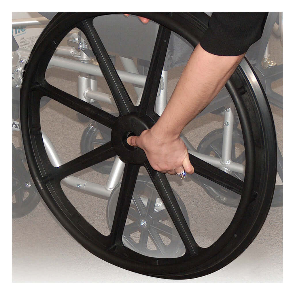 Wheelchair rear wheel being removed by hand, showing black mag-style spoke wheel detaching from silver frame
