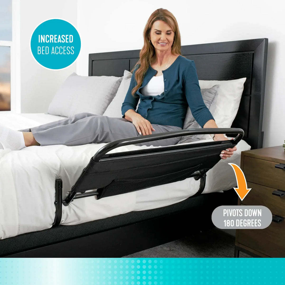 Stander 30" bed rail with padded pouch shown pivoted down flat alongside a bed while a woman sits on the mattress edge