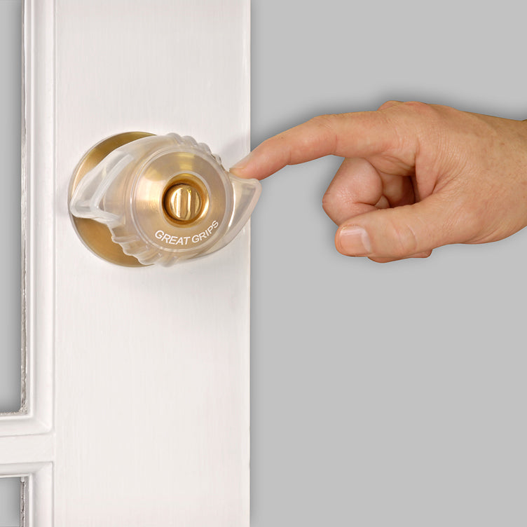 Door knob grip cover in clear plastic installed over a brass knob on a white door, with a hand reaching to turn it