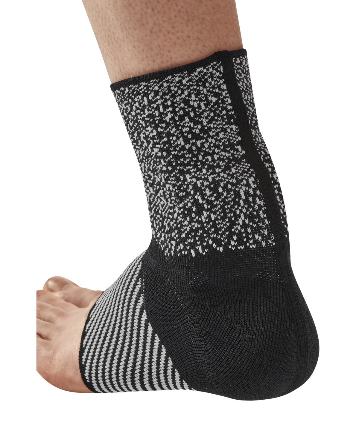 Ankle sleeve in black and gray knit fabric worn on a bare foot and lower leg, showing heel and open-toe design