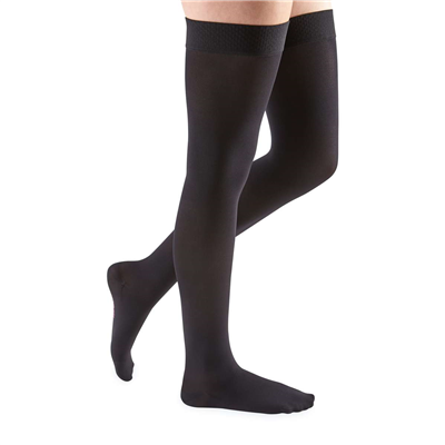 Thigh-high compression stockings in black, closed toe, with silicone top band, shown on a person's legs against a white