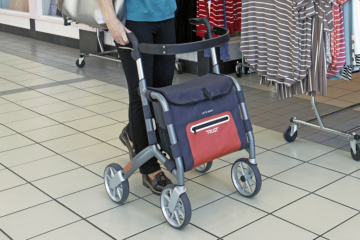 Rollator with navy and red storage bag being pushed through a shopping mall by a person wearing black pants