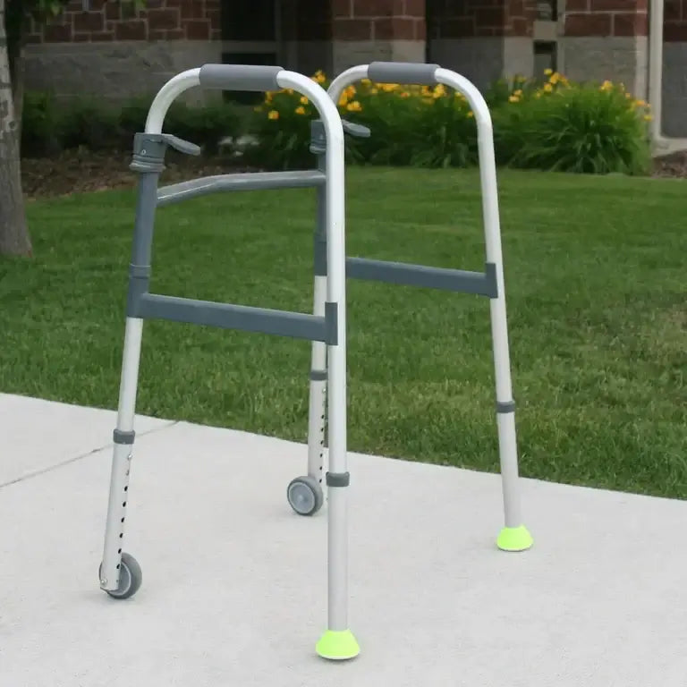 Walker with two front wheels and yellow-green tennis ball glides on rear legs, shown on outdoor concrete path