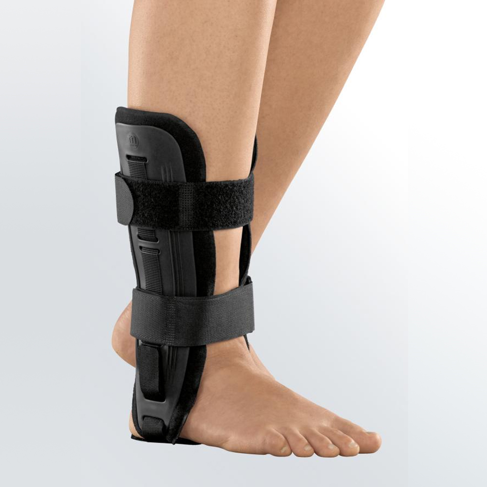 Ankle brace with rigid black shell and two hook-and-loop straps worn on a bare left foot and lower leg
