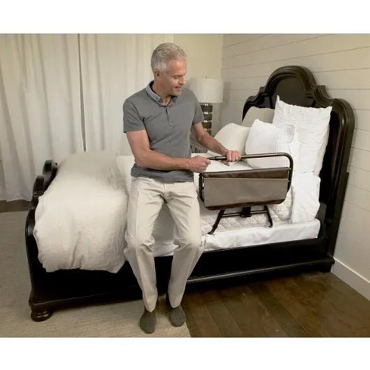 Bed rail with organizer pouch attached to a dark wood bed, with a man sitting on the bed's edge gripping the rail handle