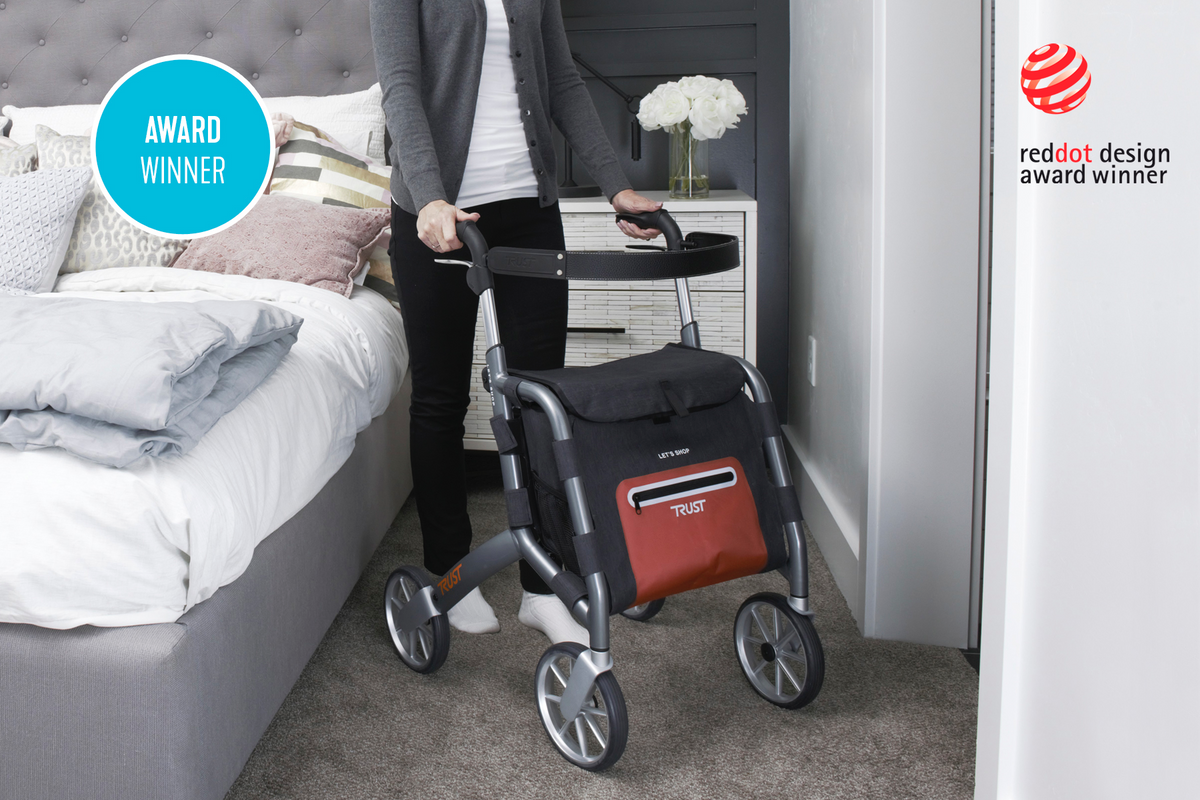 Rollator walker with tray and storage bag being used by a person in a bedroom setting, Red Dot Design Award winner