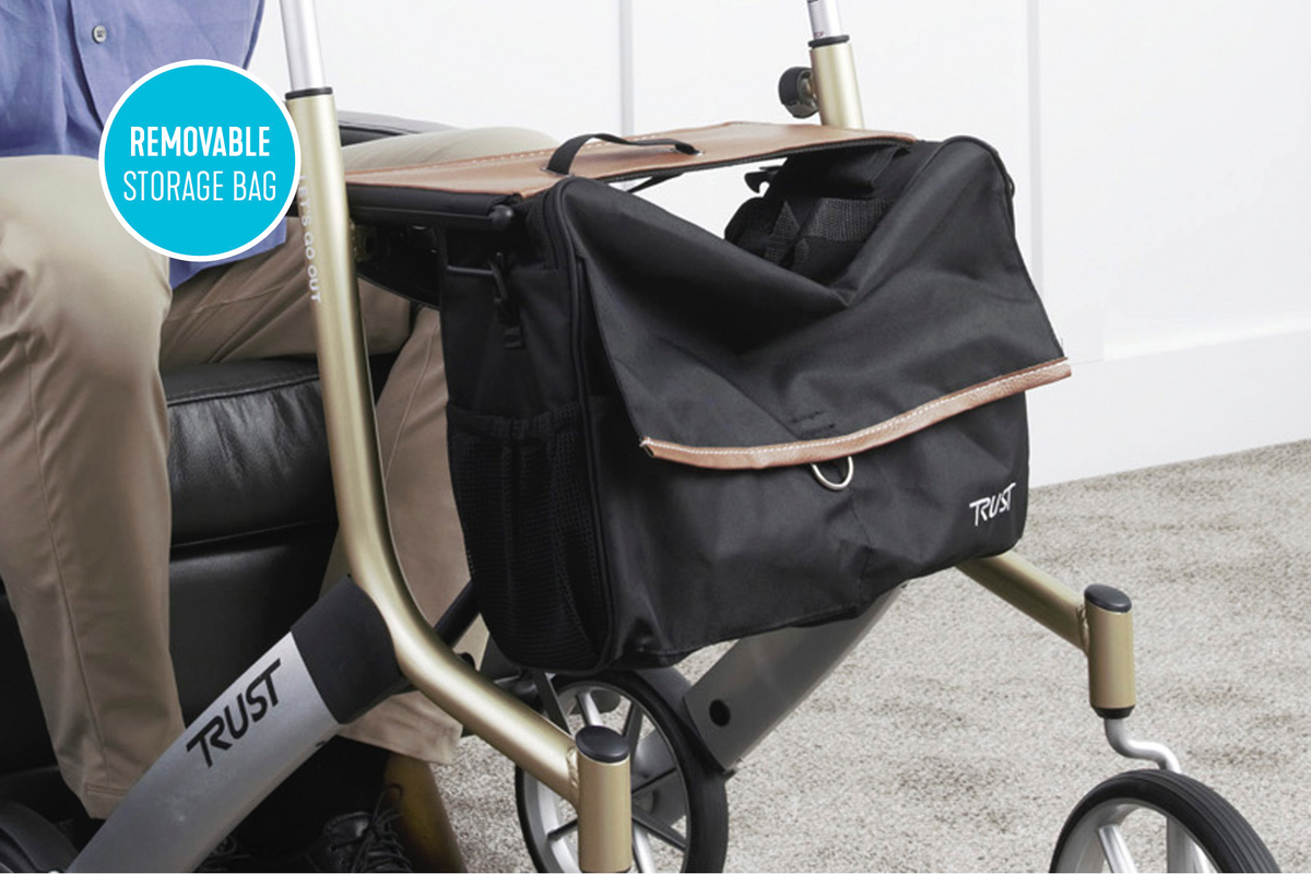Rollator with removable black storage bag attached beneath the padded seat, shown with a seated user