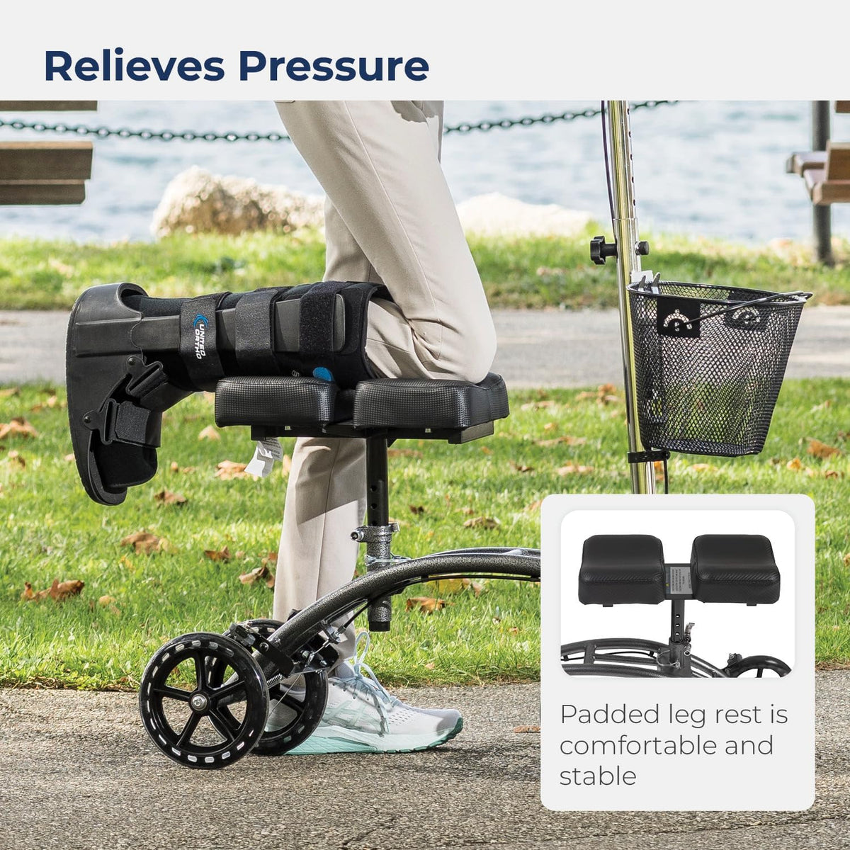 Knee walker with dual padded leg rest and front basket, shown in use outdoors on a paved path near grass and water