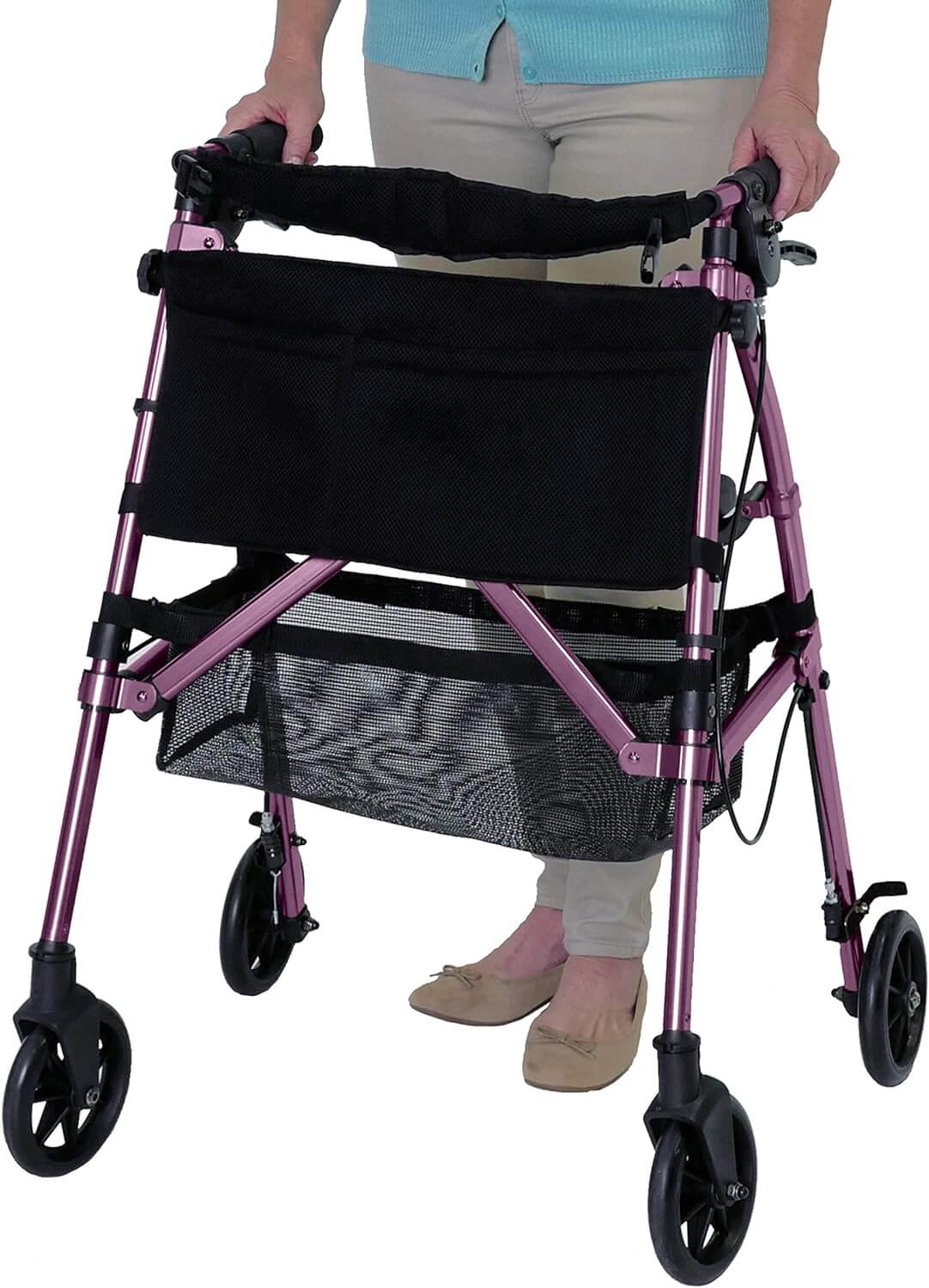 Rollator walker in pink with four wheels, hand brakes, padded seat, and black mesh storage bag, used by a woman