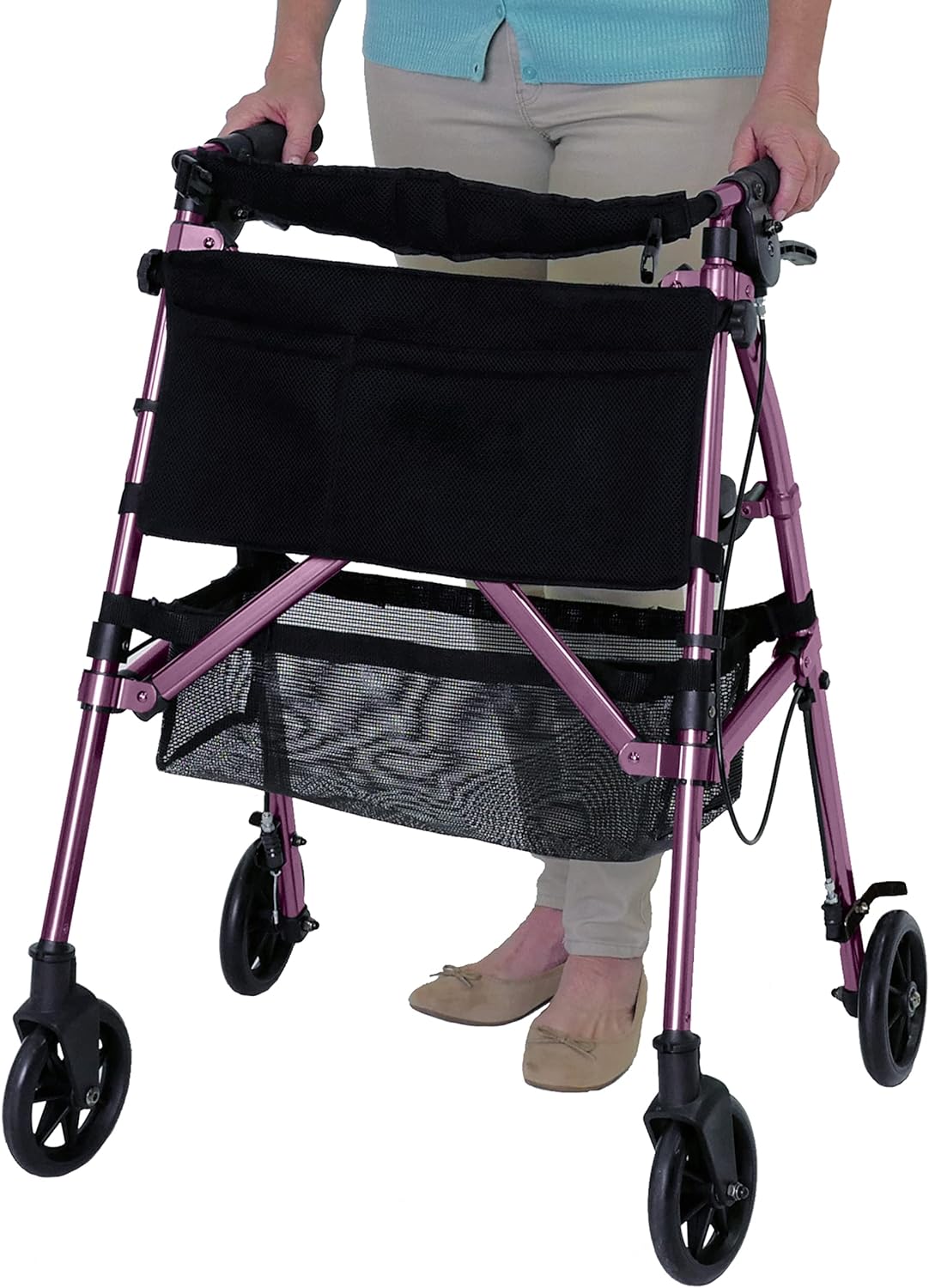 Rollator walker in pink with four wheels, hand brakes, padded seat, black storage bag, and lower mesh basket, used by a woman