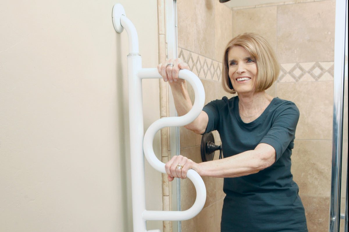 Curve grab bar with S-shaped white handholds mounted at shower entrance, shown with smiling older woman gripping both handles