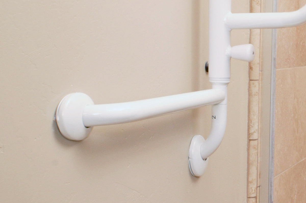 Grab bar with curved white finish mounted on a beige bathroom wall near a tiled shower entrance