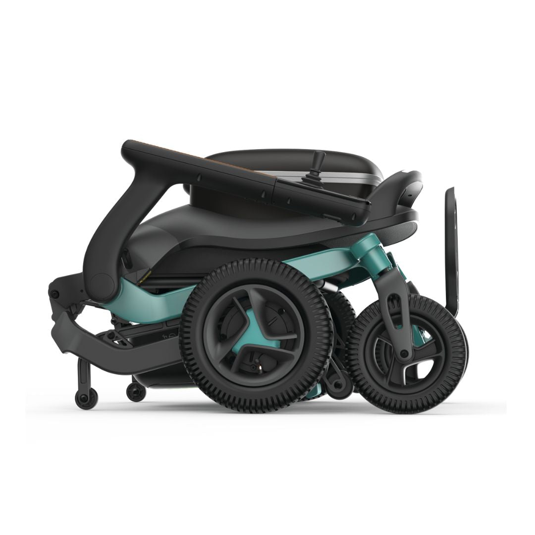 Power wheelchair folded flat, showing teal frame, black seating, joystick controller, and all-terrain wheels from a side view