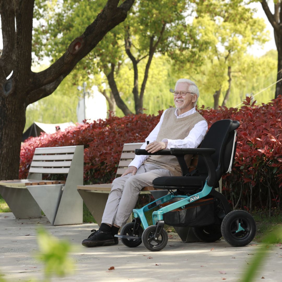 Golden Ally folding power wheelchair with teal frame and black seat, shown with smiling older man riding outdoors on a park
