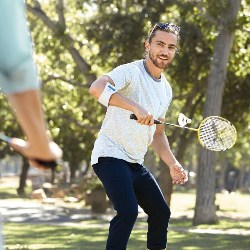 Elbow strap worn by smiling man playing badminton outdoors in a sunny park