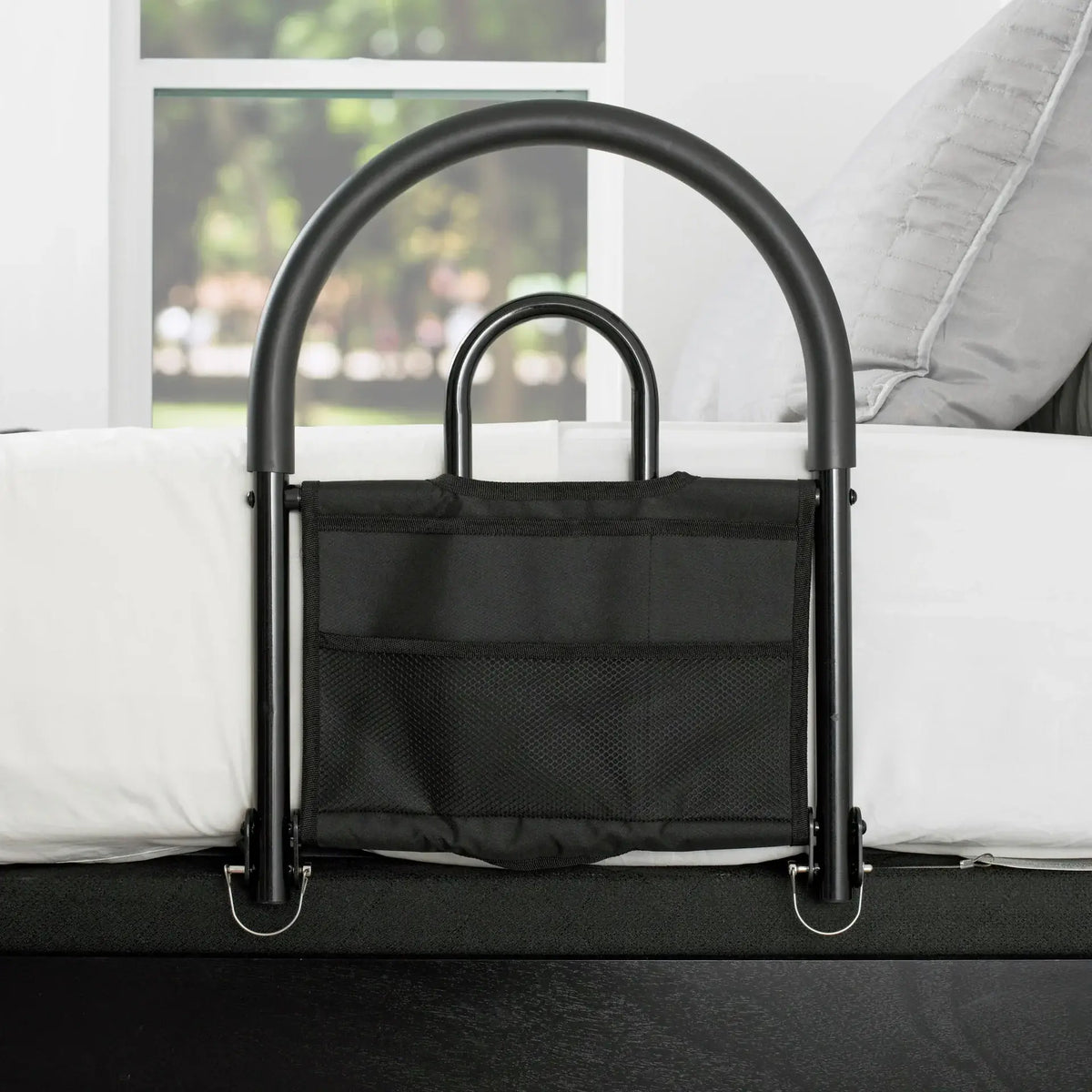 Bed rail with arched black steel frame, inner grab handle, and attached black fabric storage organizer, mounted on a white