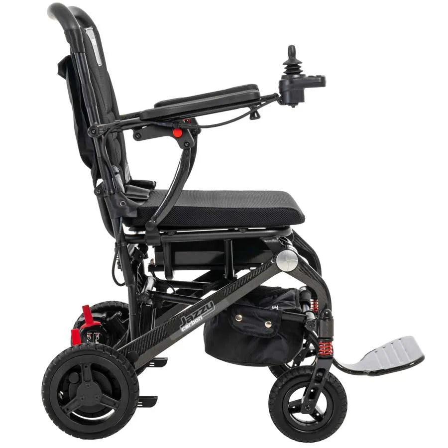 Jazzy Carbon portable power chair shown from the side, featuring joystick controller, black frame, red accents, and footrest