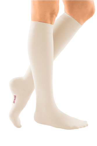 Compression socks in beige worn on legs, knee-high closed toe style with small red logo on foot