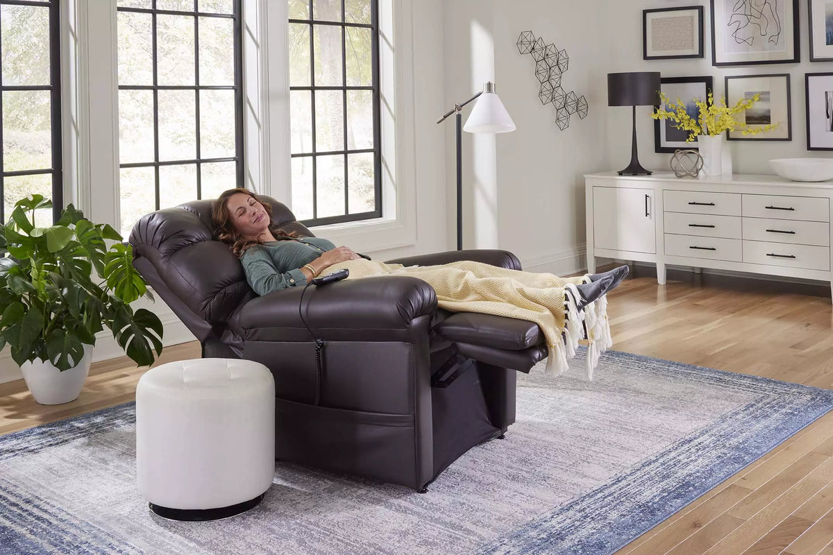 Power lift recliner in dark brown leather shown fully reclined with woman resting under a blanket in a modern living room