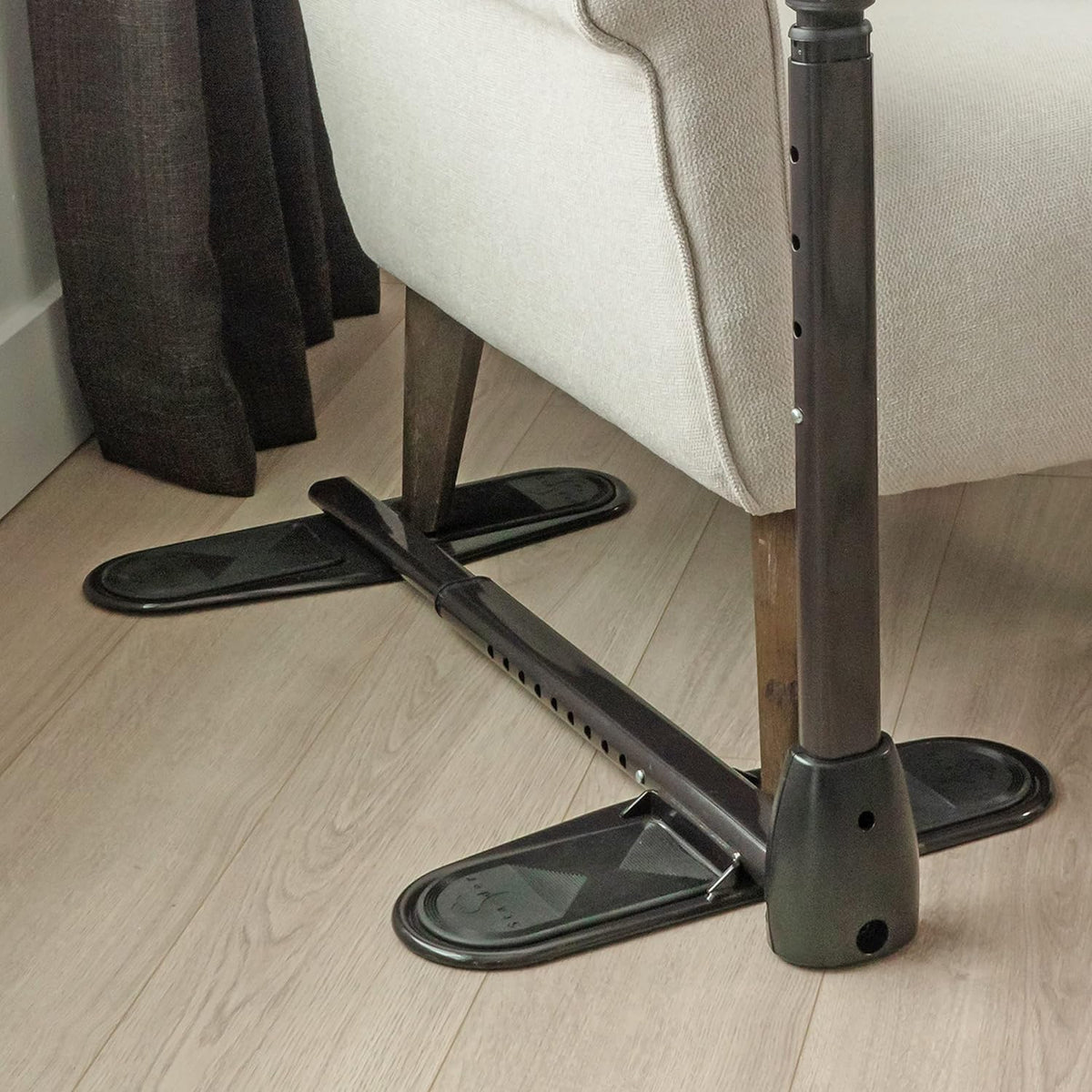 Couch cane base with cross-shaped adjustable metal shaft and wide oval non-slip feet resting on hardwood floor beside a sofa