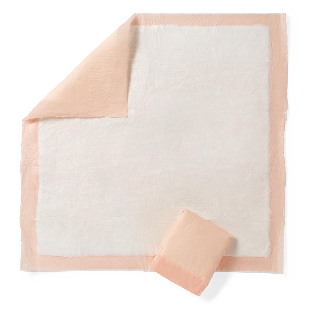 Disposable underpad laid flat showing white absorbent top and peach backing, with a second pad folded beside it
