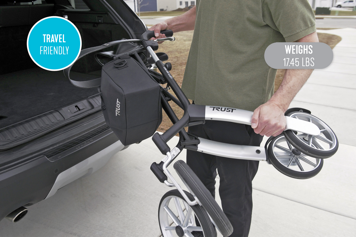 Rollator being lifted into a vehicle trunk by a person outdoors, shown folded and lightweight for travel