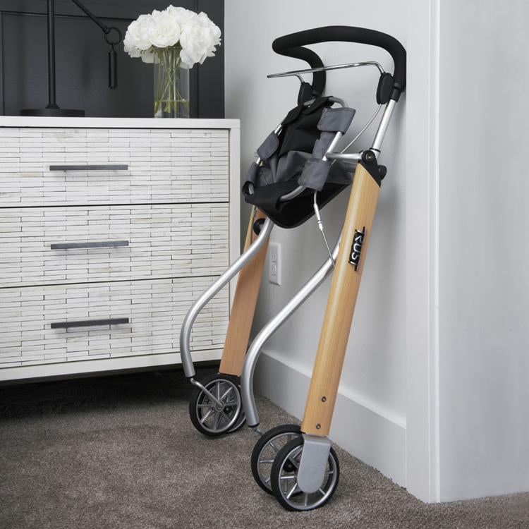 Indoor rollator with wood-tone legs, silver aluminum frame, black padded handle, and gray carry bag, folded and leaning