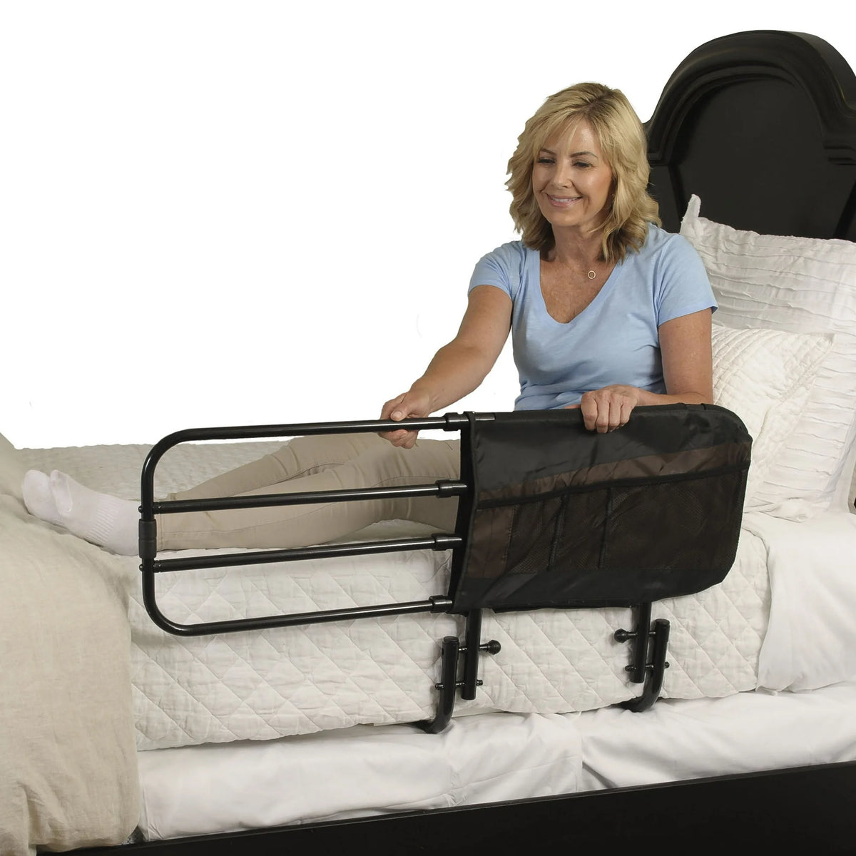 Bed rail with black metal frame and attached storage pouch secured to mattress edge, shown with woman sitting up in bed