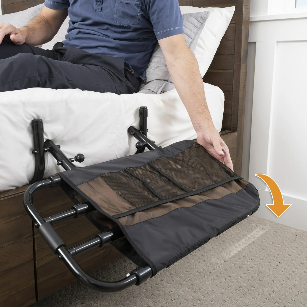 Bed rail with folding mesh organizer pocket attached to bed frame, shown in use by seated man with arrow indicating