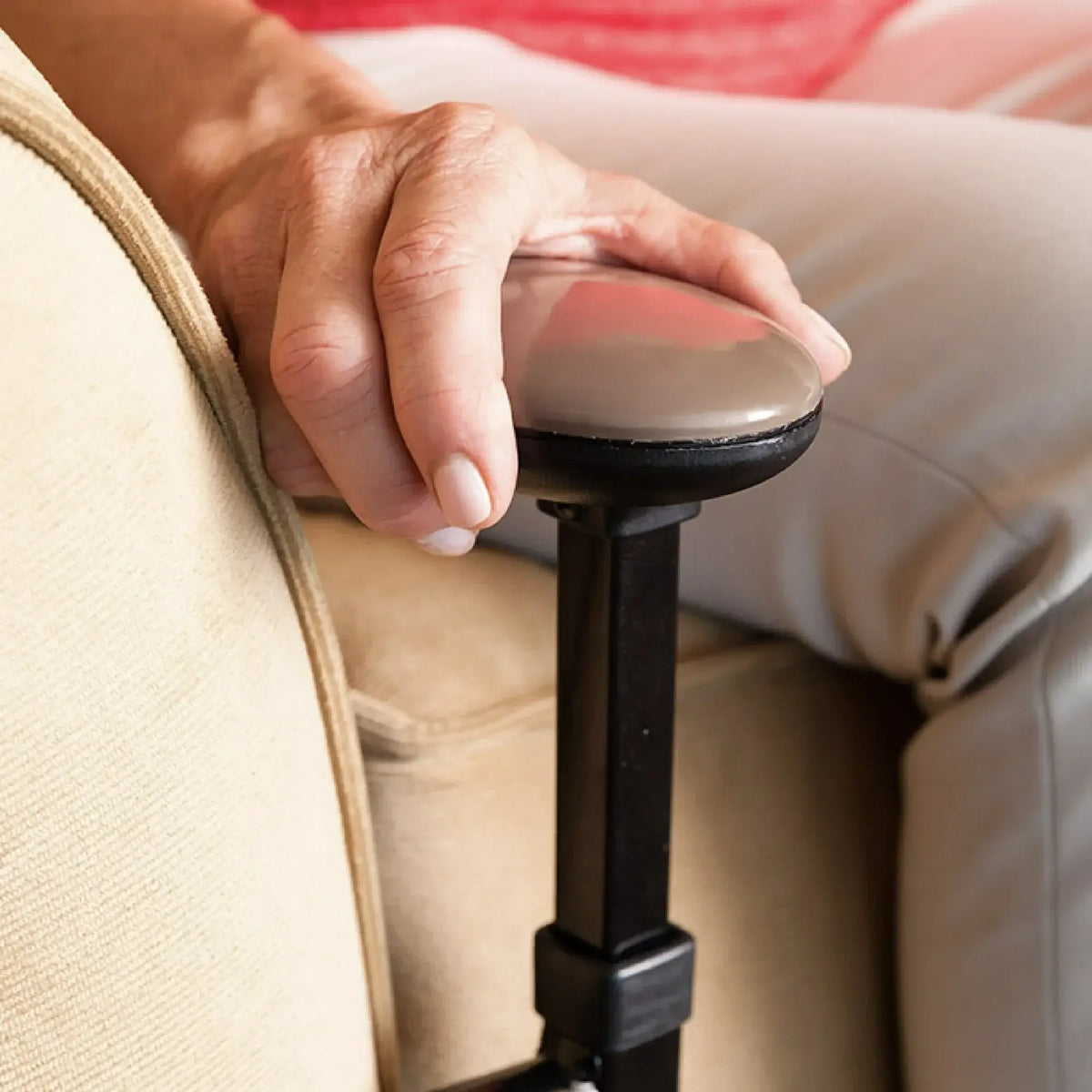 Couch stand assist handle with round grip, black metal frame tucked beside sofa cushion, shown with person's hand resting on