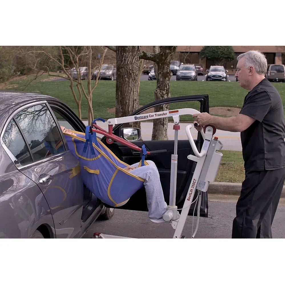 Car transfer mobile floor lift being used by caregiver to transfer patient in sling from vehicle in outdoor parking lot