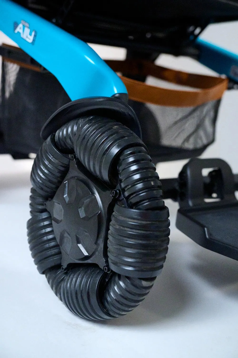 Power wheelchair close-up of a large black ribbed rubber rear wheel with blue frame and under-seat storage basket visible