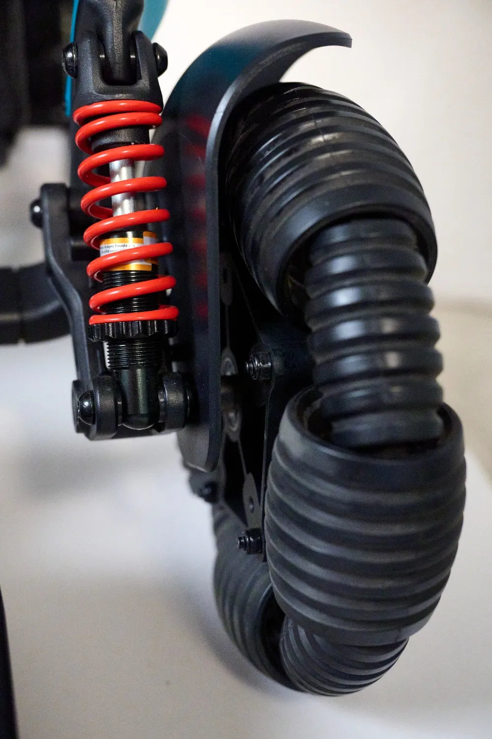 Power chair rear wheel close-up showing ribbed rubber tire, black fender, and red coil spring suspension assembly