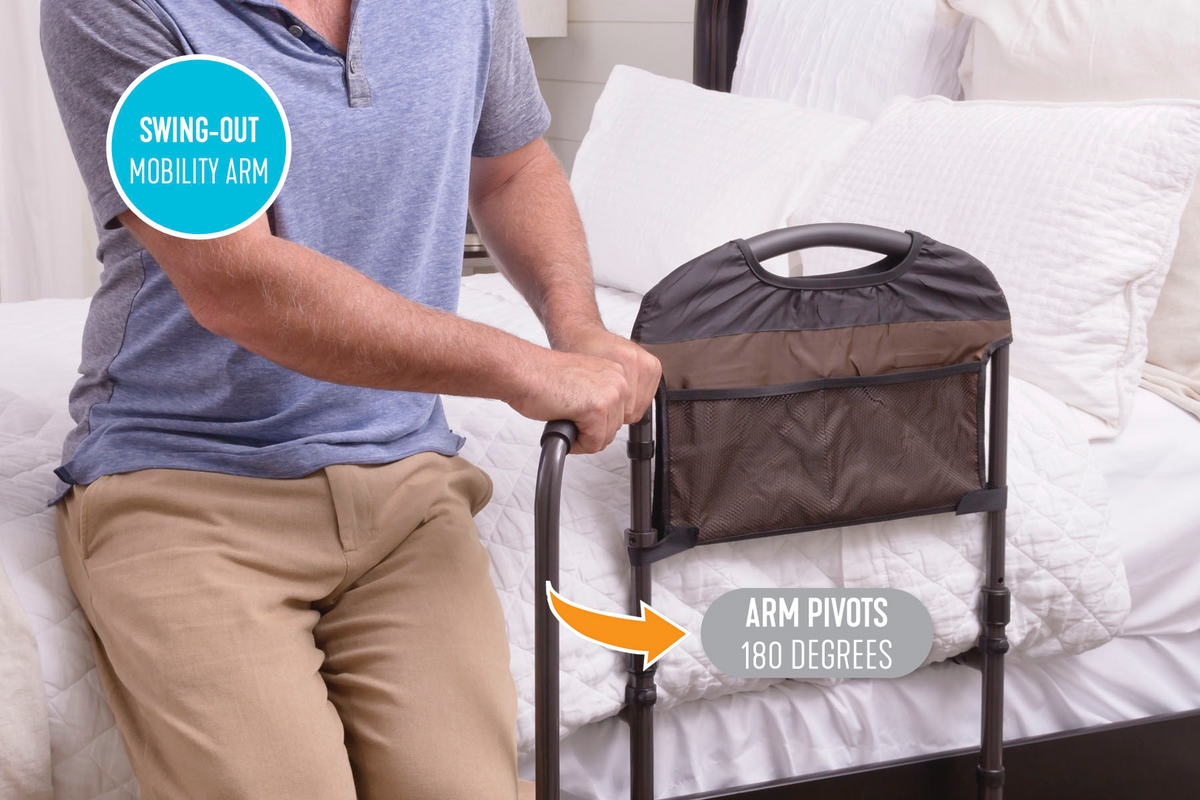 Bed rail with swing-out mobility arm and storage pouch, shown with a man gripping the handle while seated on the edge of a