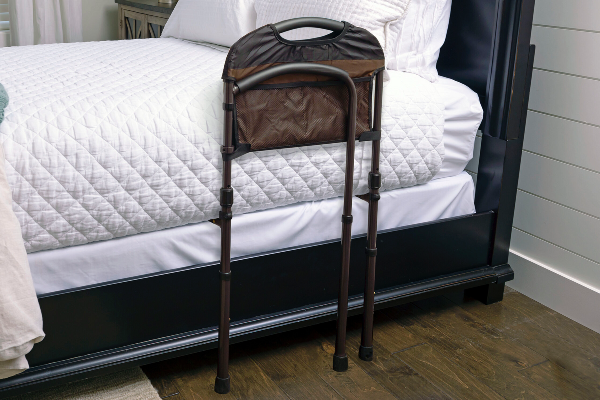 Bed rail with brown padded handle and mesh storage pocket, positioned alongside a mattress on a dark wood bed frame