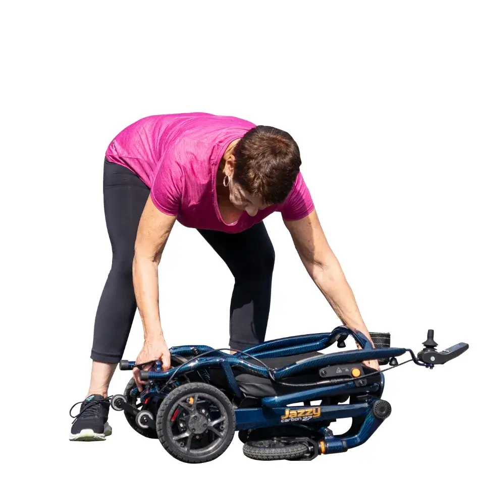 Jazzy Carbon 27 power wheelchair folded flat, with a woman in a pink shirt lifting it from the ground