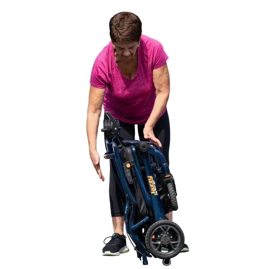 Jazzy Carbon power wheelchair folded compactly while woman in pink shirt demonstrates its lightweight foldable design